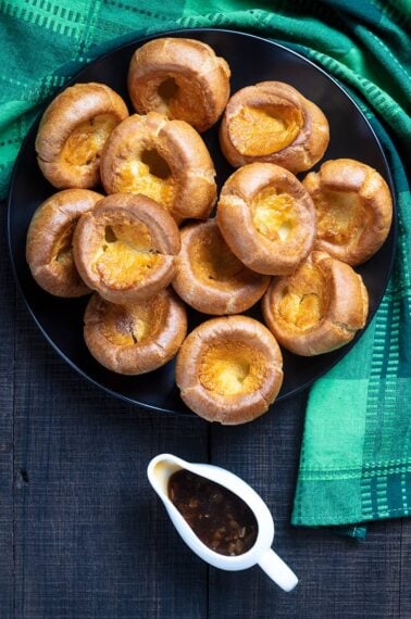 Traditional Yorkshire Pudding on a black serving plate with brown gravy, a green tablecloth underneath