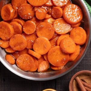 close up large serving dish with Candied Yams and wooden spoon, cinnamon sticks cayenne pepper and walnuts beside