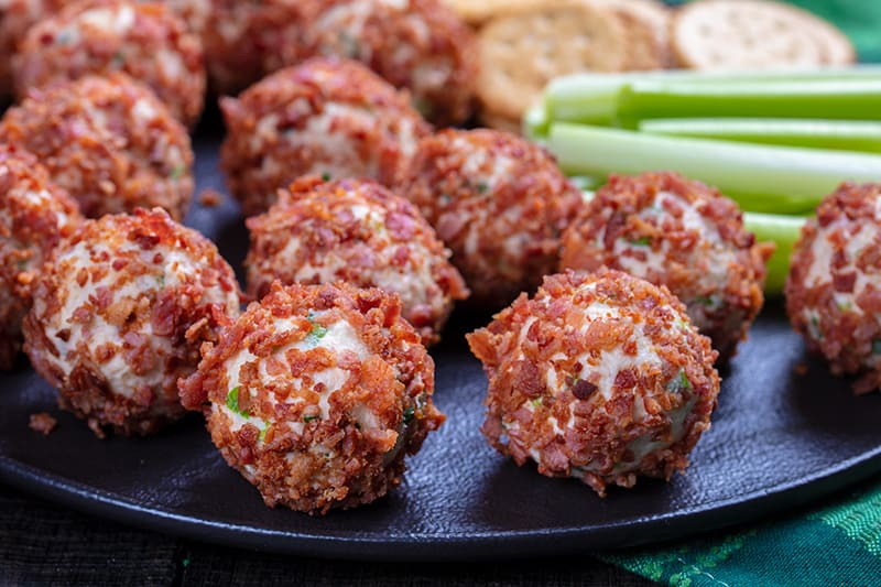 large black dinner plate with Cheese Ball rolled on bacon and celery sticks