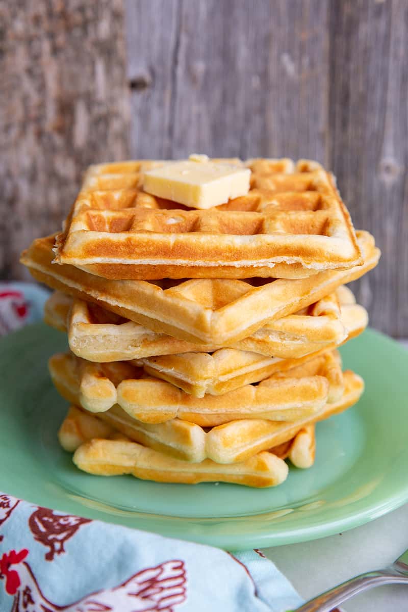 close up green small plate with stack of fluffy Classic Waffle topped butter and maple syrup