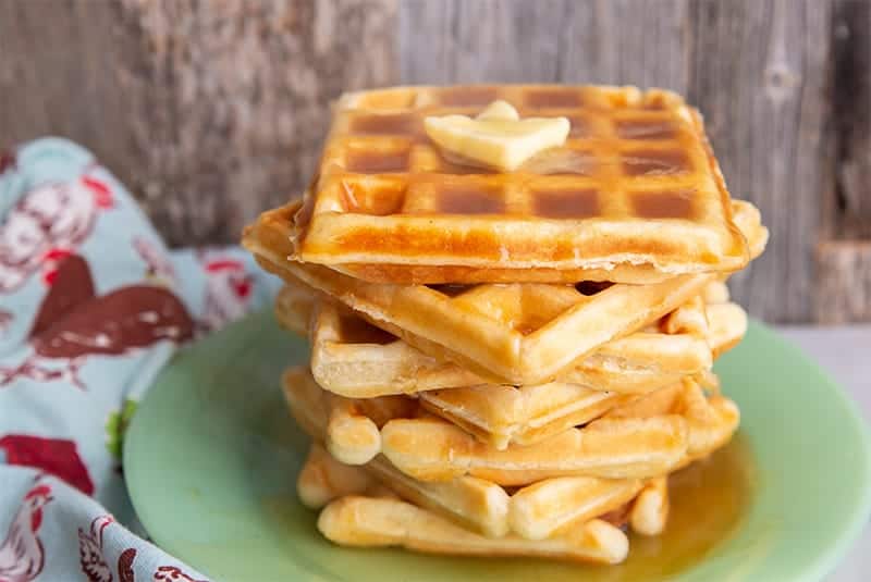 green small plate with a stack of fluffy Classic Waffle topped butter and maple syrup