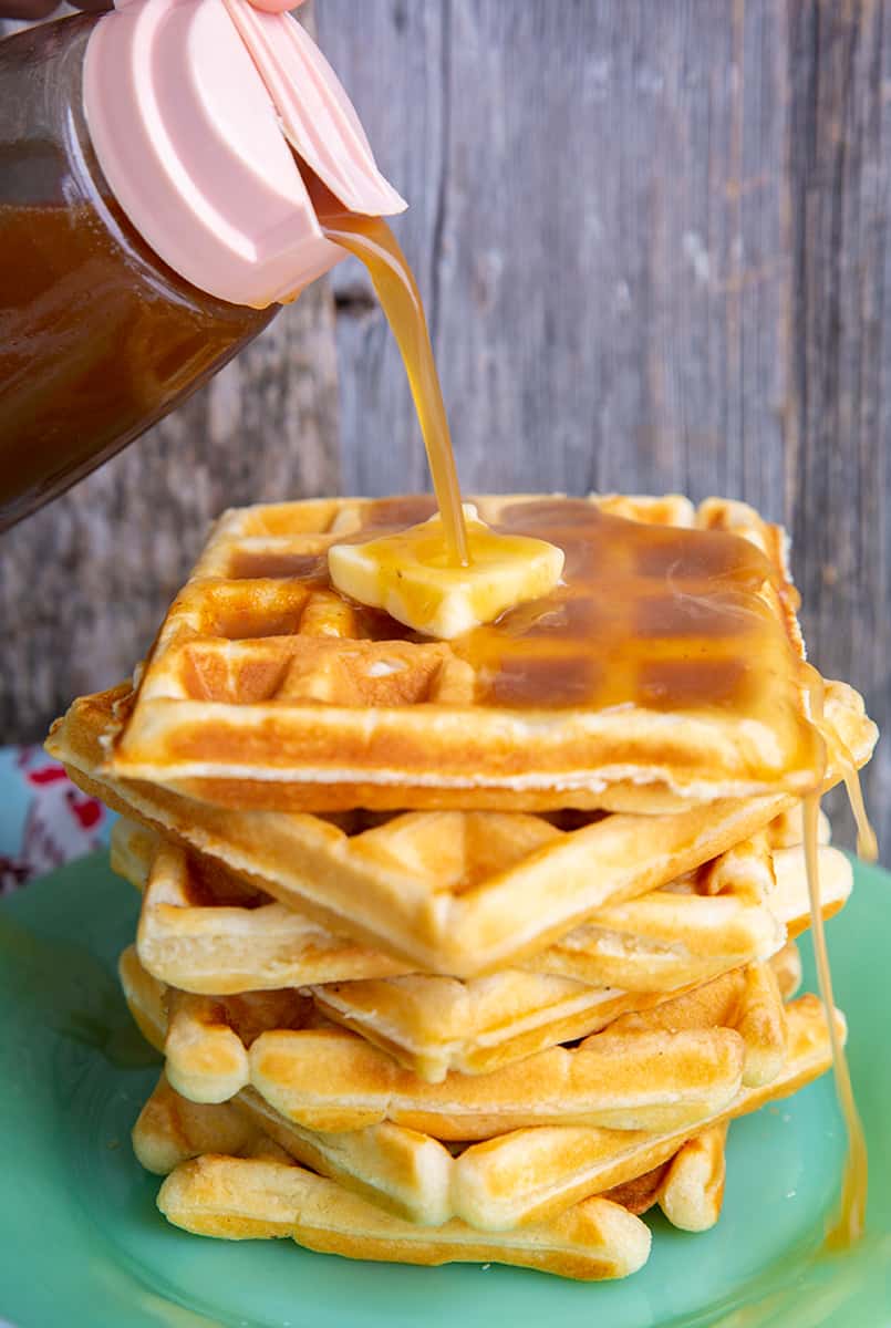adding maple syrup on top of fluffy Classic Waffles with butter butter in green small plate