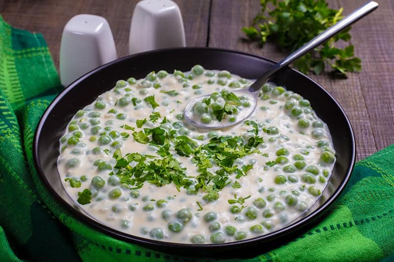 green tablecloth underneath a black serving plate with Creamed Peas sprinkled with parsley