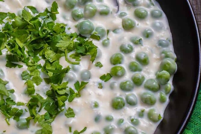 close up green tablecloth underneath a black serving plate with Creamed Peas sprinkled with parsley