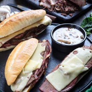 close up Cheesy Mushroom French Dip Sandwiches and a cup of gravy on a large serving plate