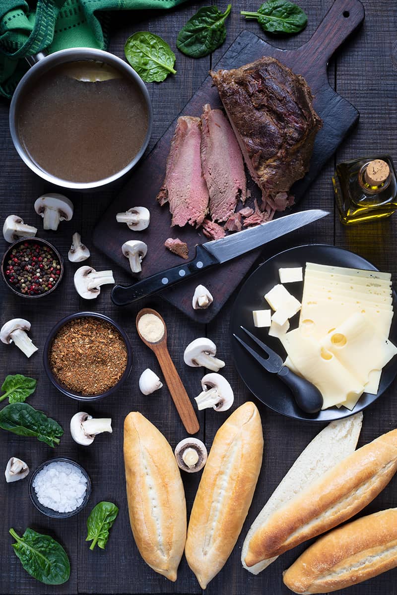 French Dip Sandwich ingredients on wooden cutting board and dark wood background