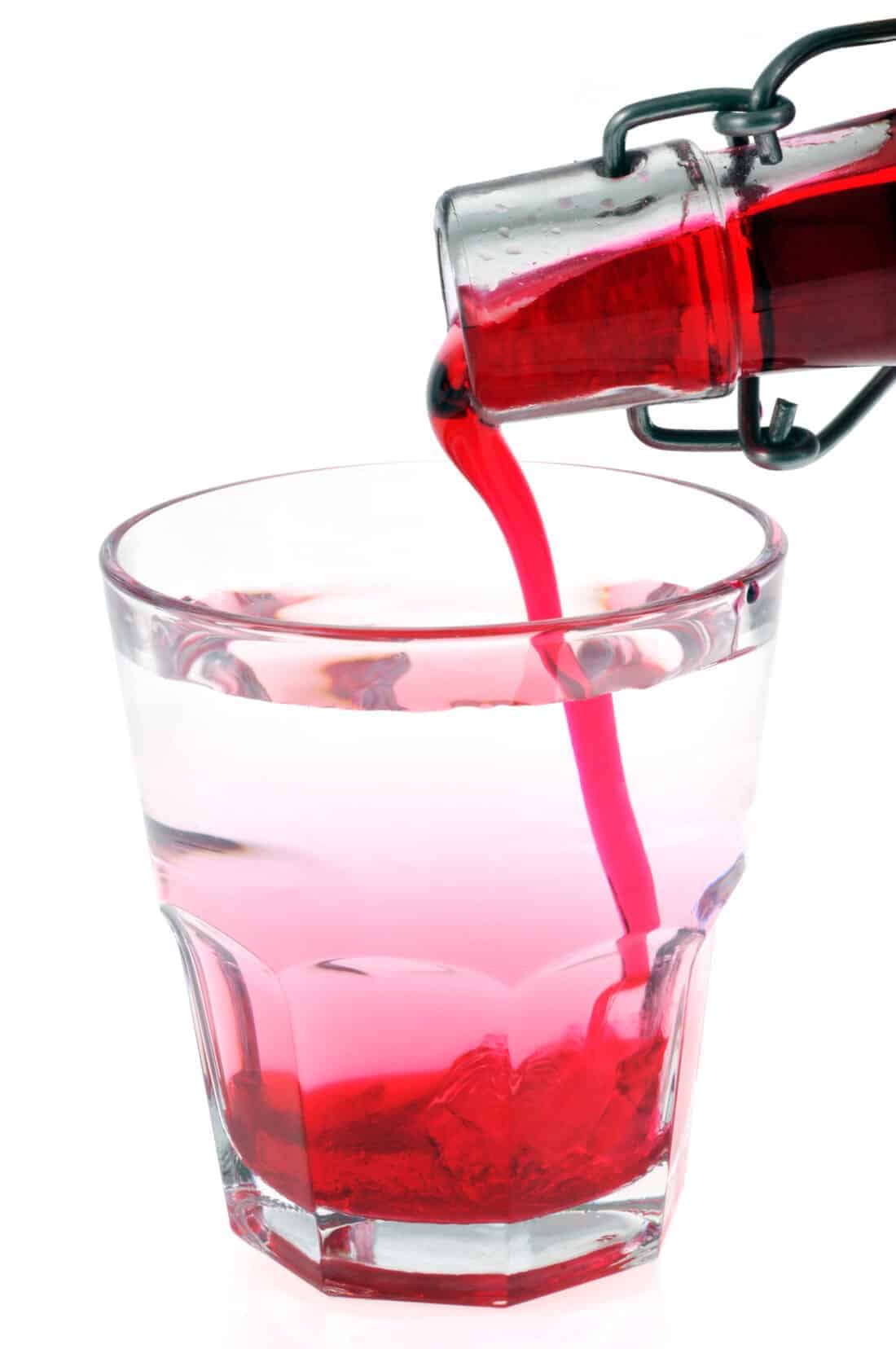 adding pomegranate juice mixed on a glass with sugar and water for homemade grenadine