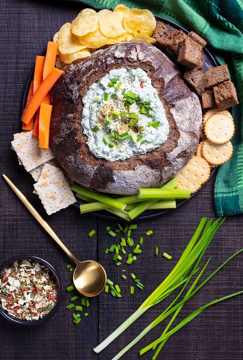 Knorr Spinach Dip in a bread bowl with some crisp crackers, potato chips, homemade pita chips and veggies, gold spoon and some green onions at the side