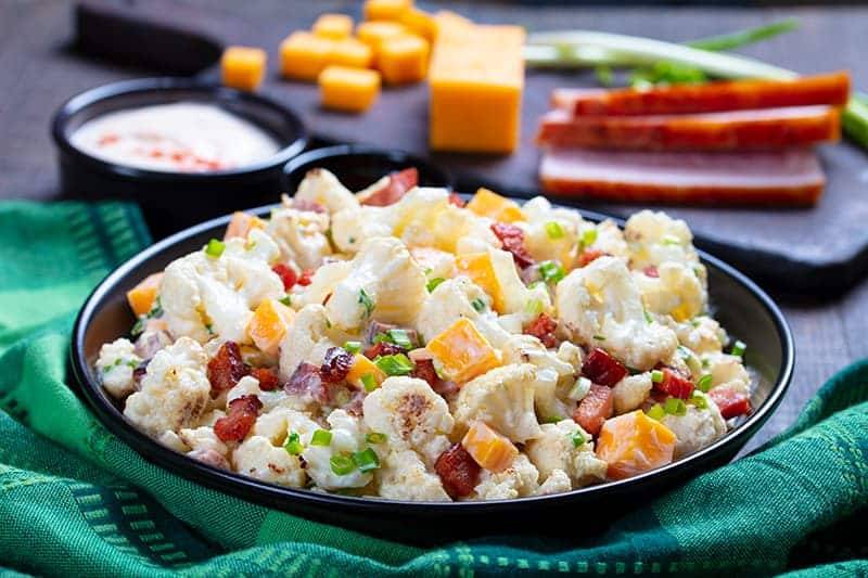 green tablecloth underneath a plate of Cauliflower Salad, ingredients on its background