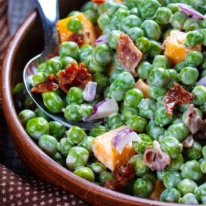 close up brown polka dot tablecloth underneath a bowl of Cheddar Bacon Green Pea Salad with a spoon