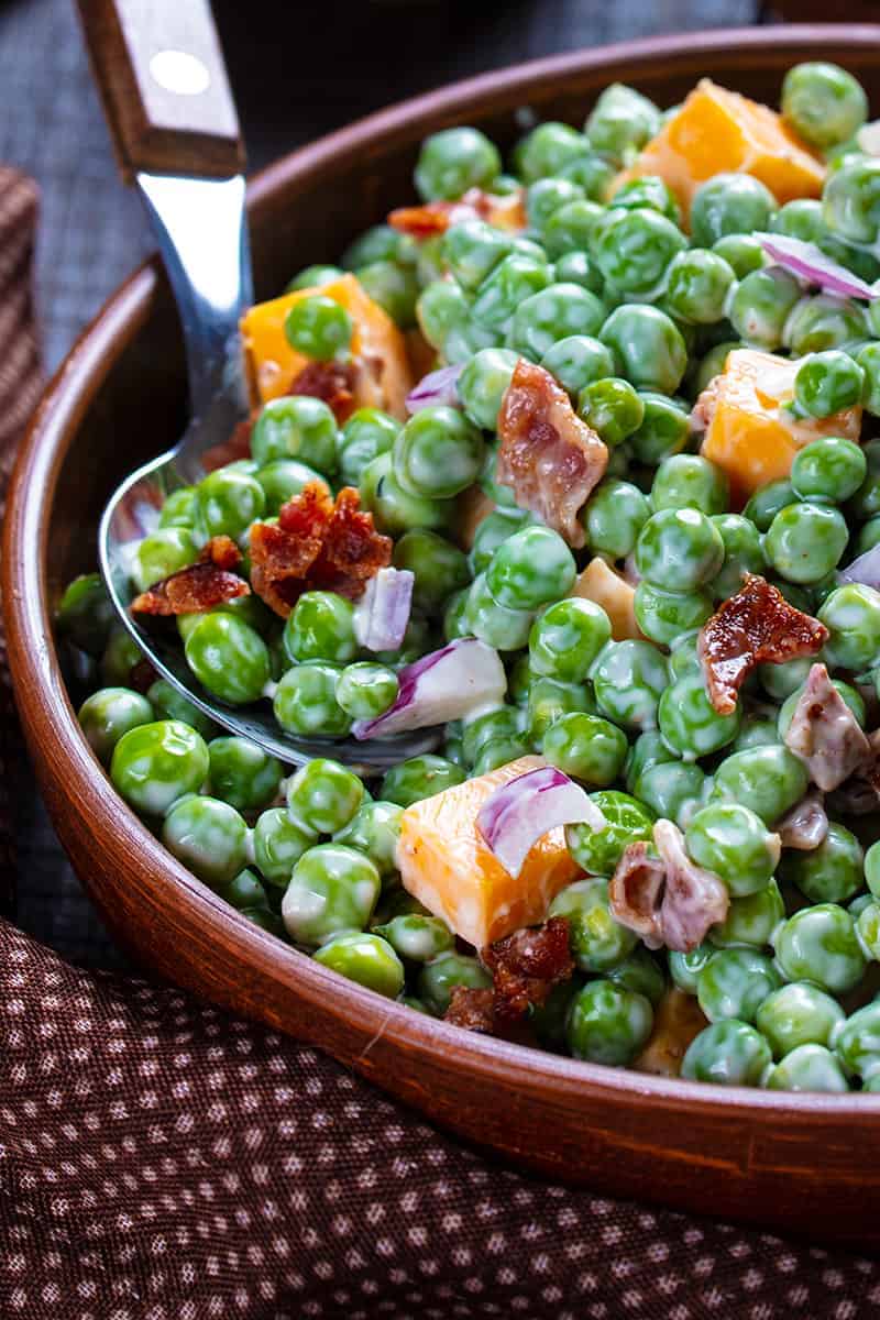 close up brown polka dot tablecloth underneath a bowl of Cheddar Bacon Green Pea Salad with a spoon