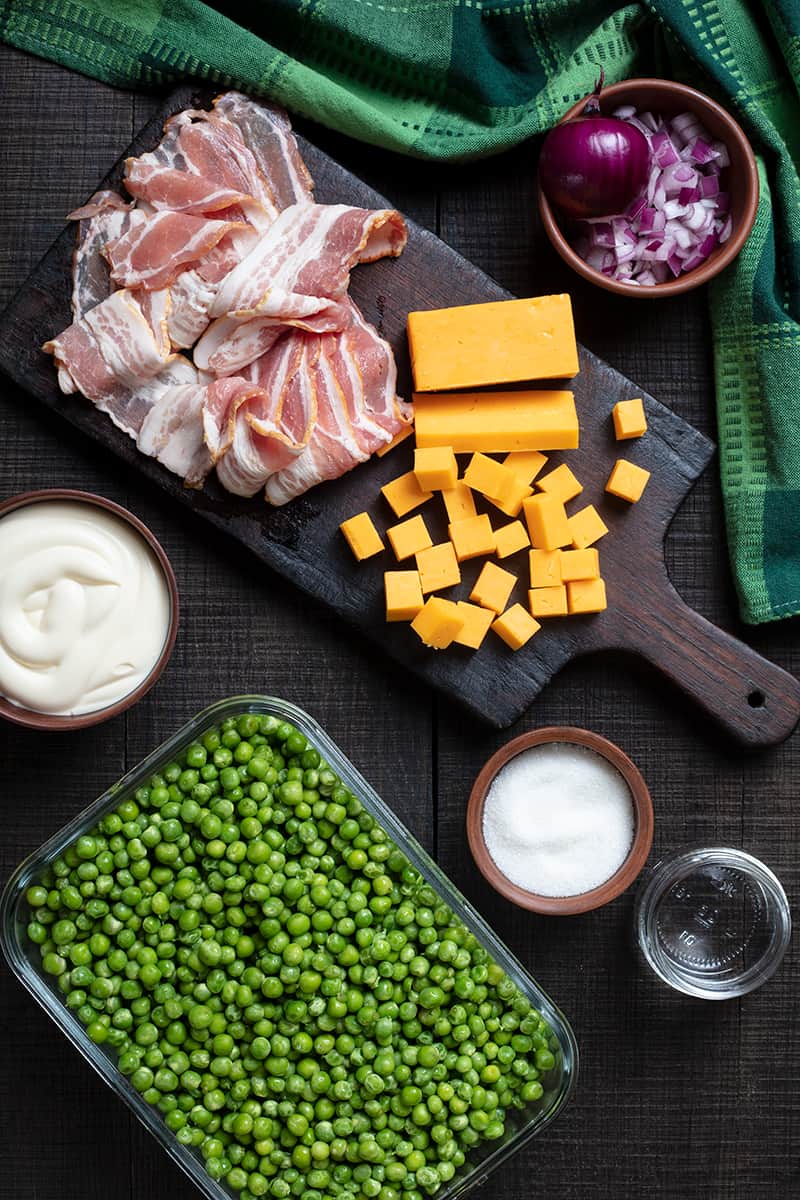 cheddar bacon green pea salad ingredients on wooden chopping board and green tablecloth at one side