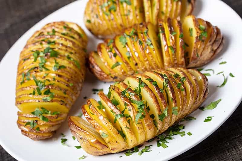 white plate with Hasselback Potatoes sprinkled with parsley flakes
