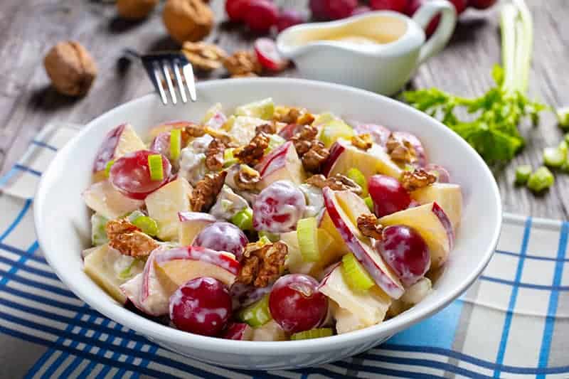 checkered blue tablecloth underneath white dessert bowl with Classic Waldorf Salad, ingredients on its background