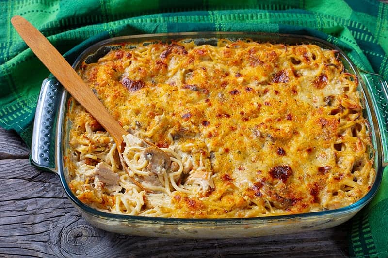 green tablecloth beside the glass baking dish full of chicken tetrazzini with wooden spoon