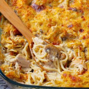 close up glass baking dish full of chicken tetrazzini with wooden spoon