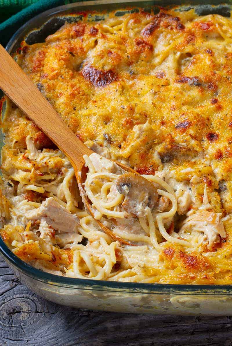 close up glass baking dish full of chicken tetrazzini with wooden spoon
