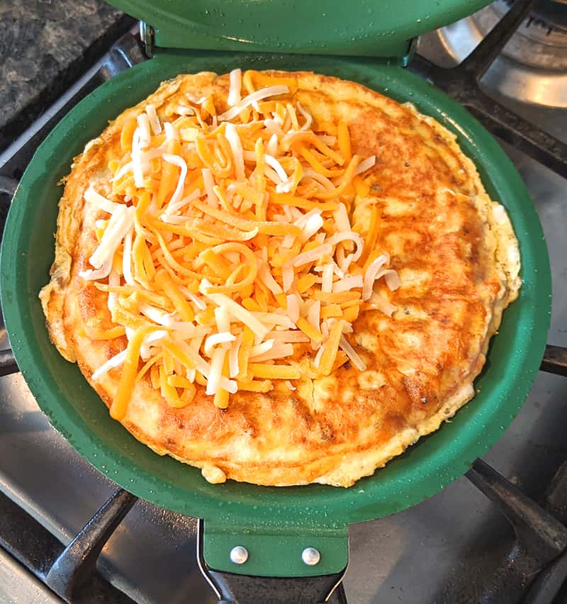 omelette with shredded cheese on top in a green color omelette or crepe pan