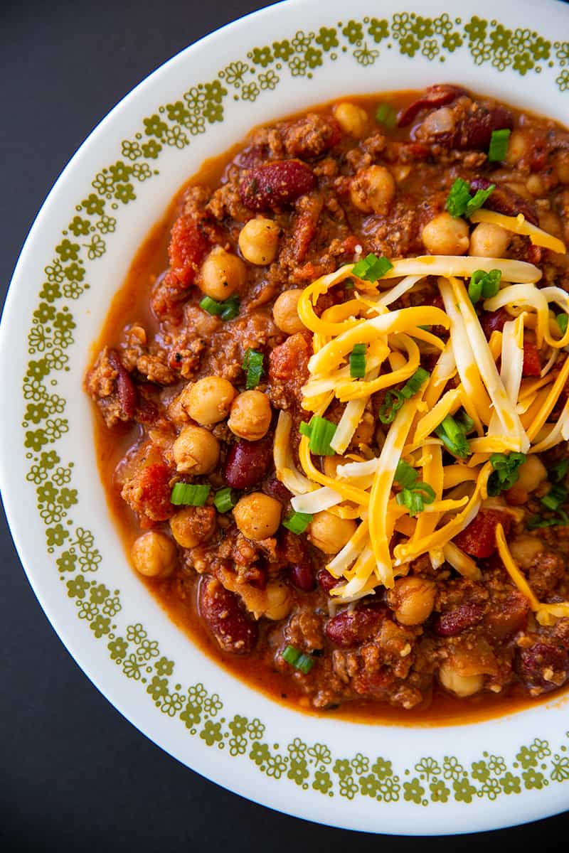 close up instant pot chili with shredded cheese on a white plate with tiny gold floral design on side