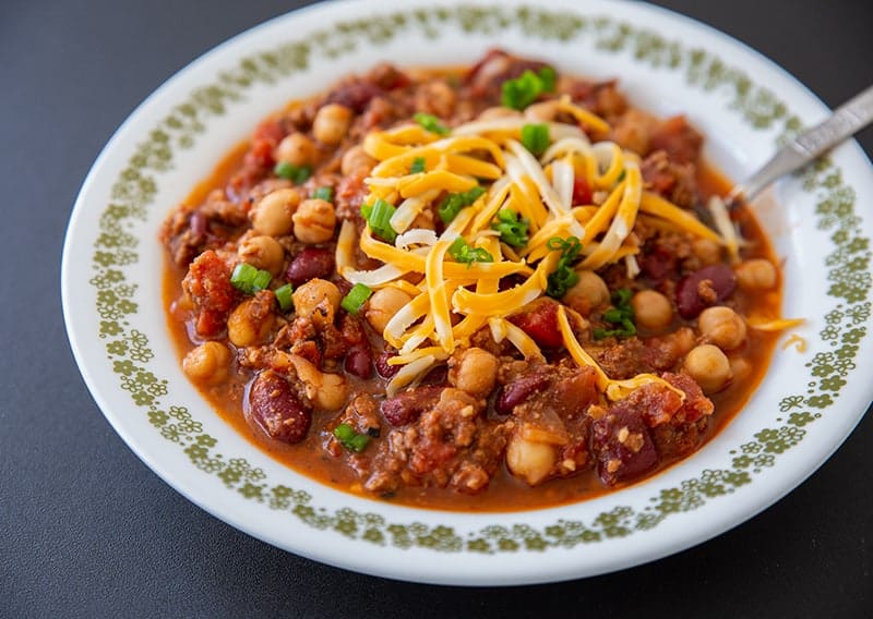 instant pot chili with shredded cheese on a white plate with tiny gold floral design on side and a spoon