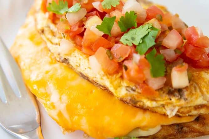 Taco Omelette top with pico de gallo and cilantro on a white plate with fork