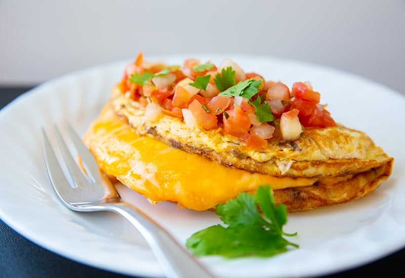Taco Omelette top with Pico de gallo and cilantro on a white plate with fork