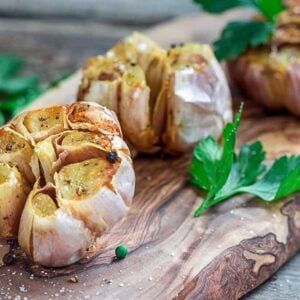 whole roasted garlic with intact skin garnished with some parsley leaves on a piece of wood background