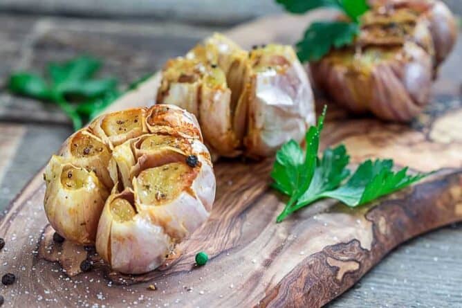 whole roasted garlic with intact skin garnished with some parsley leaves on a piece of wood background