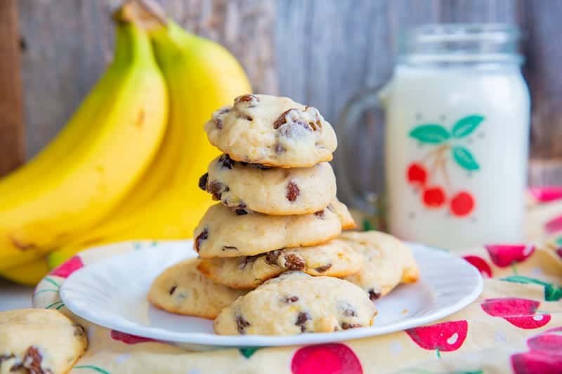 soft and fluffy banana cookies layered in a white plate, ripe bananas and milk in a mason jar with handle on its background