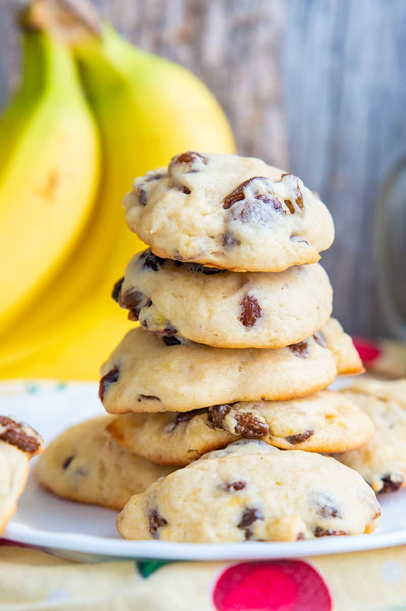 close up soft and fluffy banana cookies layered in a white plate, ripe bananas on its background