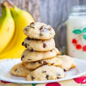 soft and fluffy banana cookies layered in a white plate, ripe bananas and milk in a mason jar with handle on its background