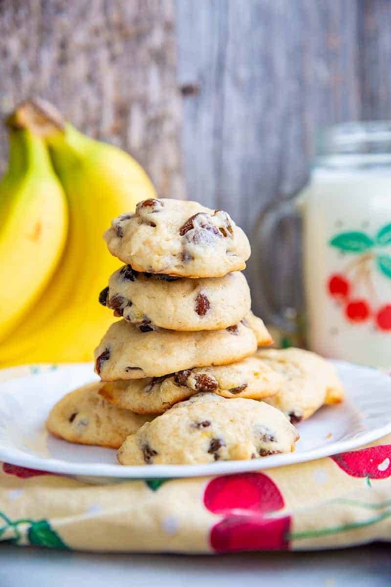 close up soft and fluffy banana cookies layered in a white plate, ripe bananas and milk in a mason jar with handle on its background