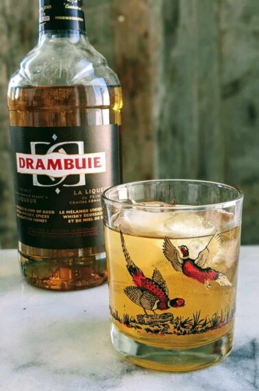 Rusty Nail cocktail on a pheasant glass with a bottle of Drambuie behind it