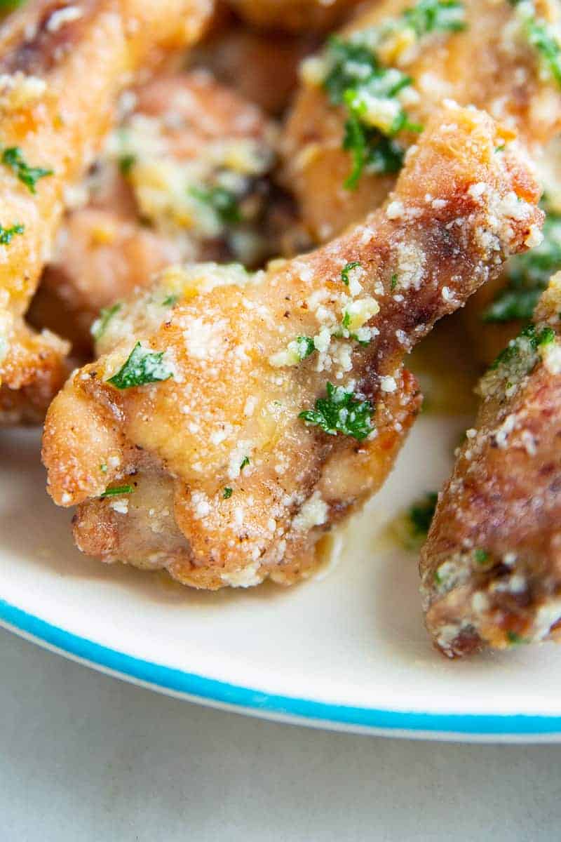 close up of one garlic Parmesan chicken wing on a white plate garnished with green parsley
