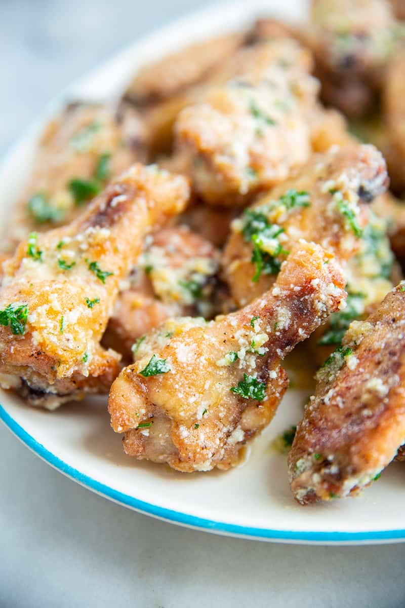 close up garlic parmesan chicken wings on a white plate garnished with green parsley