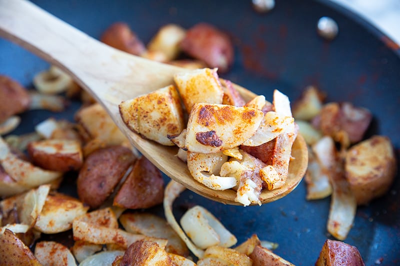 crispy pan fried potatoes and onions with paprika in a medium sized skillet with wooden spoon 