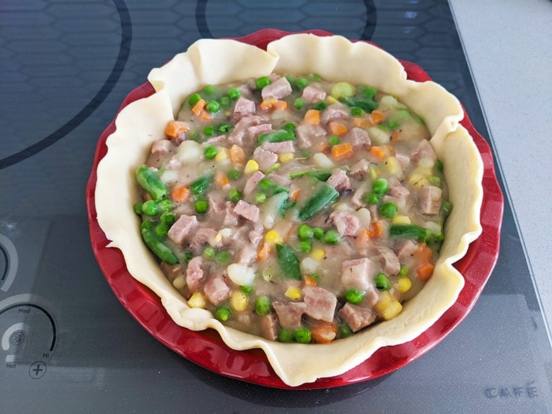 pie crust in the bottom of red pie plate with beef, vegetable and gravy filling