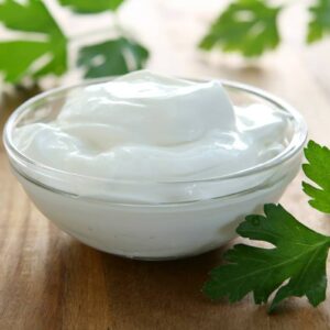 Sour Cream in a small transparent glass bowl on top of wooden table with some parsley leaves