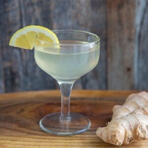 ginger martini in a coupe glass, garnished with a lemon wedge and ginger root beside it