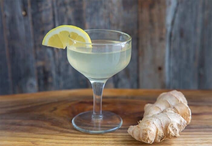 ginger martini in a coupe glass, garnished with a lemon wedge and ginger root beside it