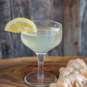 ginger martini in a coupe glass, garnished with a lemon wedge and ginger root beside it