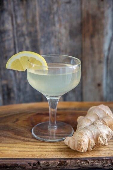 ginger martini in a coupe glass, garnished with a lemon wedge and ginger root beside it