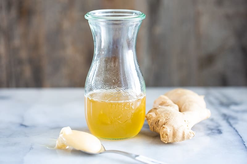 Ginger Simple Syrup in an airtight transparent glass with chuck of ginger beside it and a spoon of honey