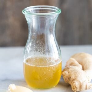 Ginger Simple Syrup in an airtight transparent glass with chuck of ginger beside it and a spoon of honey