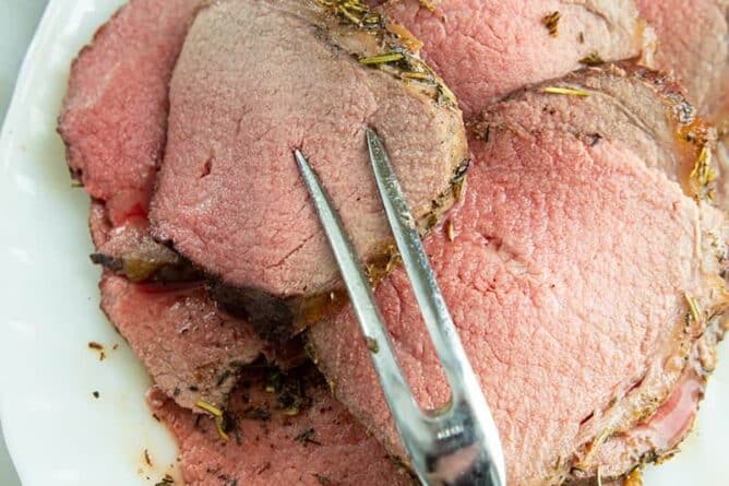 thin slices of stuffed eye of round roast in a white plate with pot fork