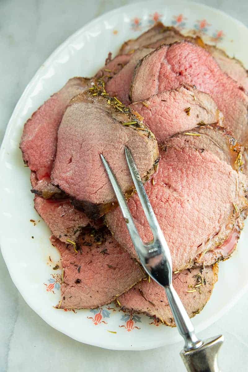 close up thin slices of stuffed eye of round roast in a white plate with pot fork