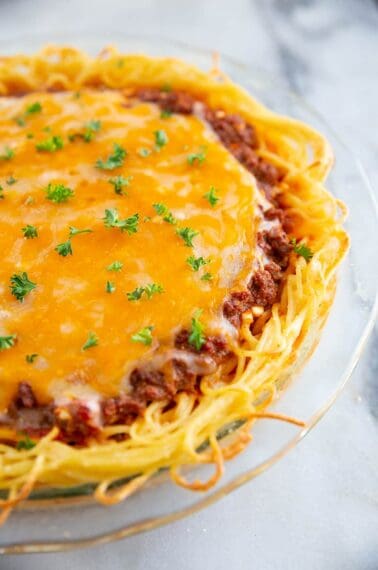 close up baked spaghetti pie on a large Pyrex plate with melted cheese on top and garnished with fresh parsley