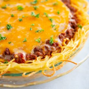 close up of baked spaghetti pie with melted cheese on top and garnished with fresh parsley