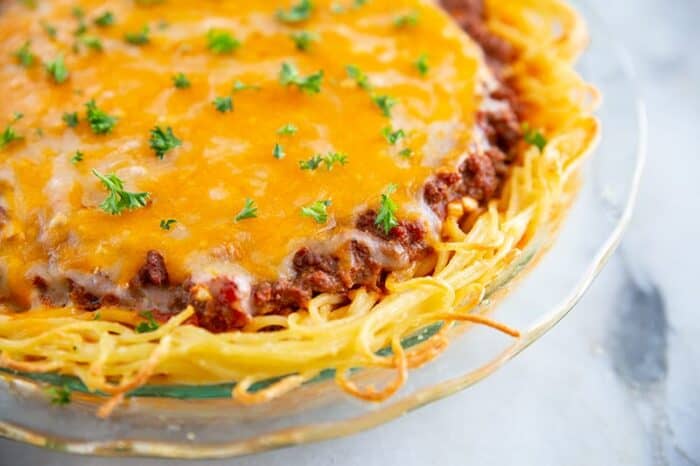 close up of baked spaghetti pie with melted cheese on top and garnished with fresh parsley