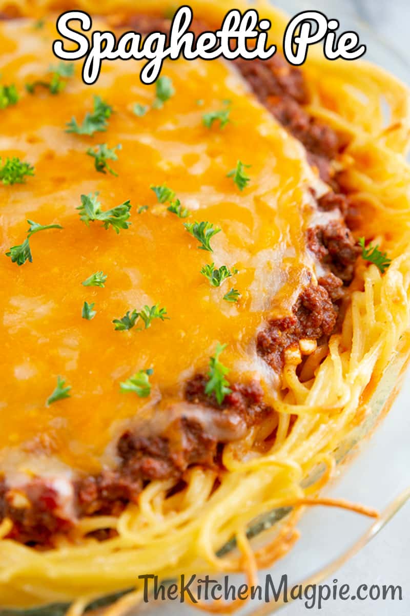 close up baked spaghetti pie on a large Pyrex plate with melted cheese on top and garnished with fresh parsley